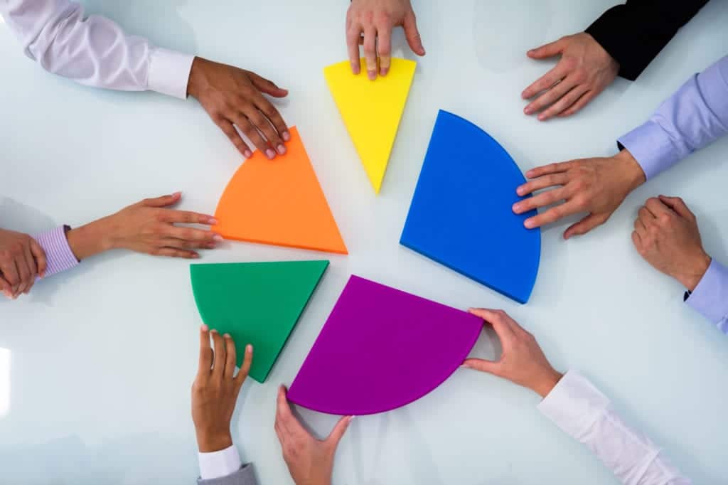 Businesspeople Hand Connecting Multi Colored Pieces Of Pie Chart On Desk