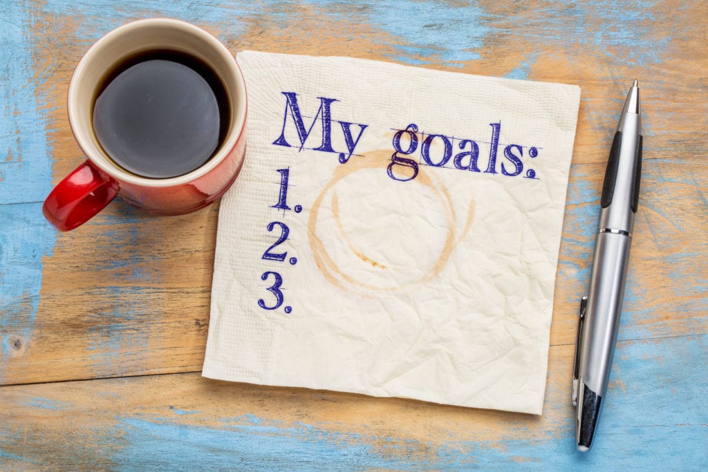 my goals list on a stained napkin against grunge wood table with  a cup of coffee